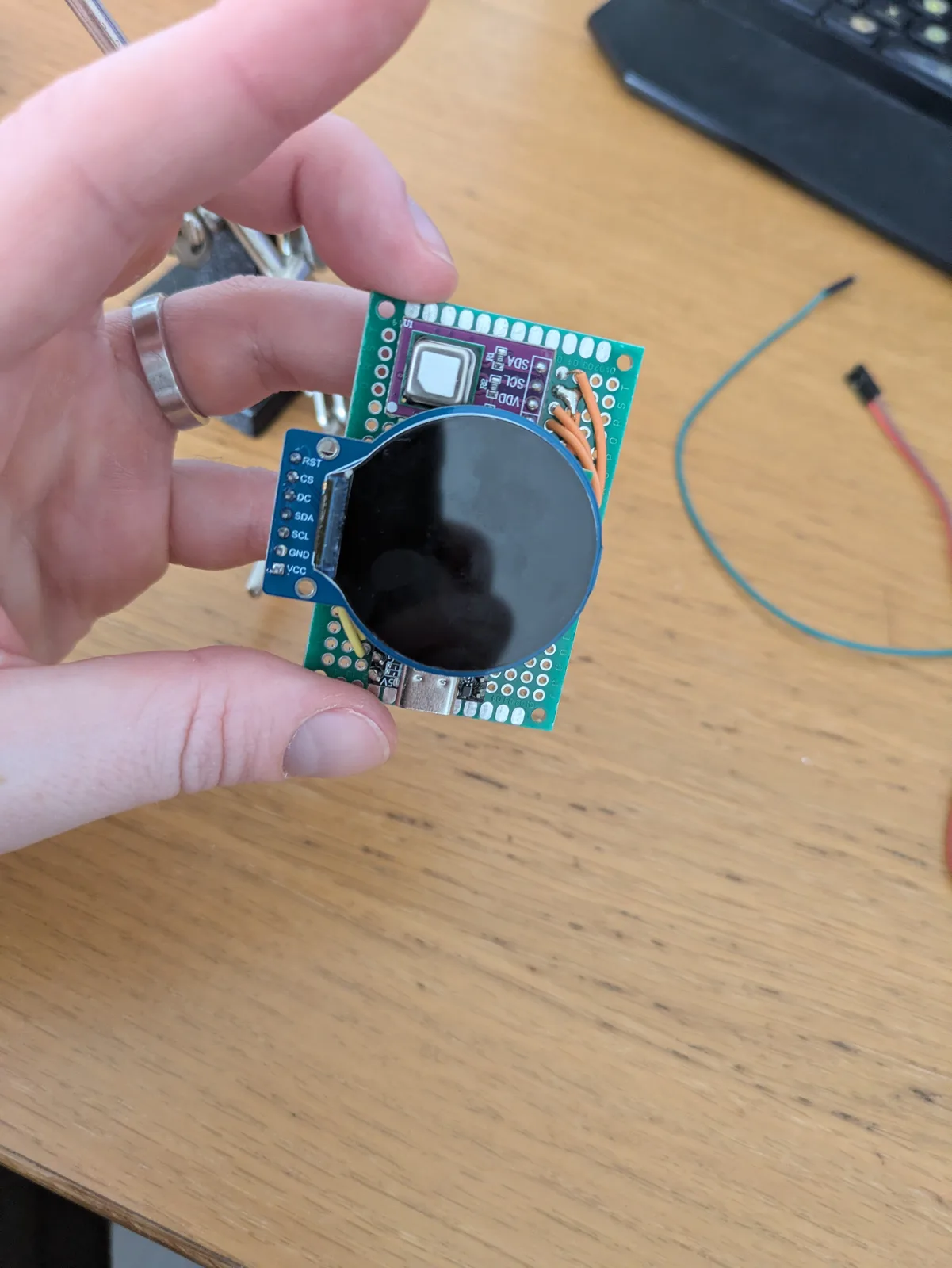 Bare assembled round display and sensor board held in one hand